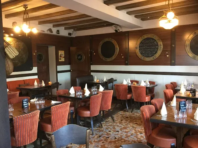 Salle du restaurant Au Quai des Brumes, tables dressées, sièges rouges et décoration marine.